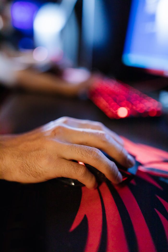 A focused hand using a gaming mouse on a vibrant mouse pad with a blurred computer setup in the background.